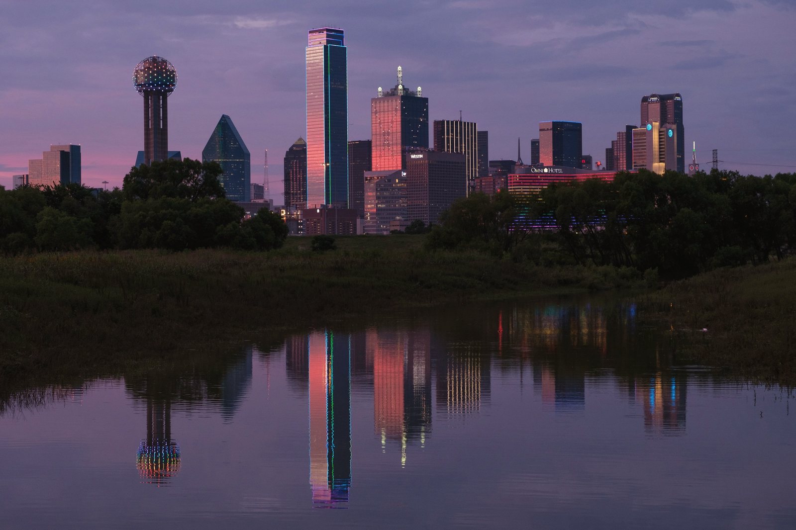 The Dallas skyline at sunset, reflected in still water.