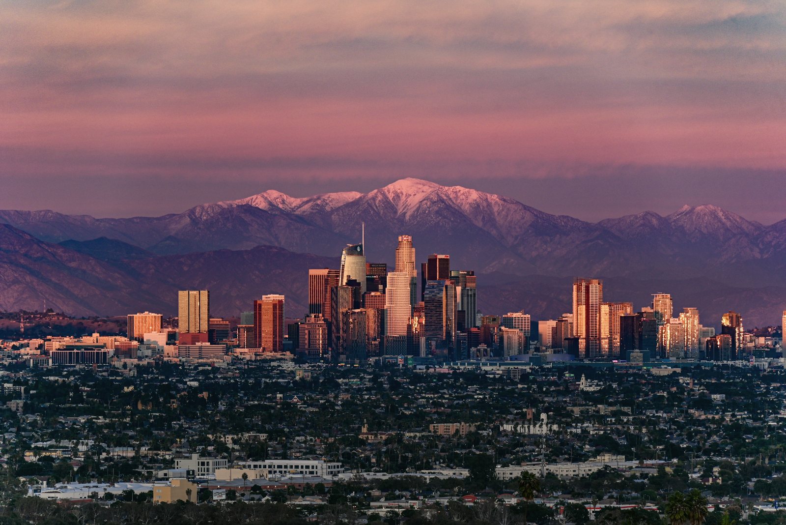 Downtown Los Angeles at low sun, with snow on the San Gabriel Mountains behind.