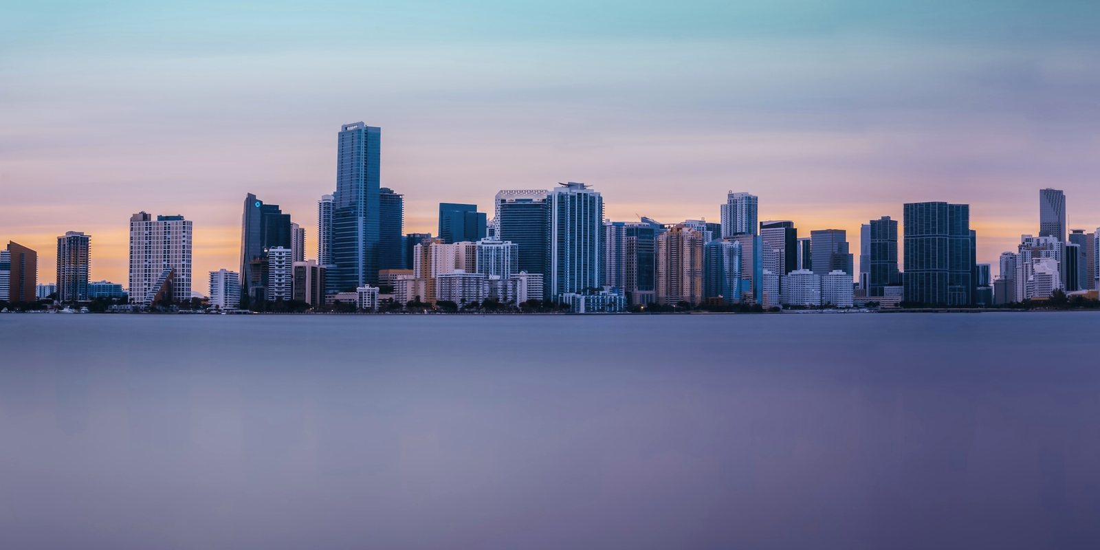 The towers of Miami seen across the still water of Biscayne Bay at dusk.