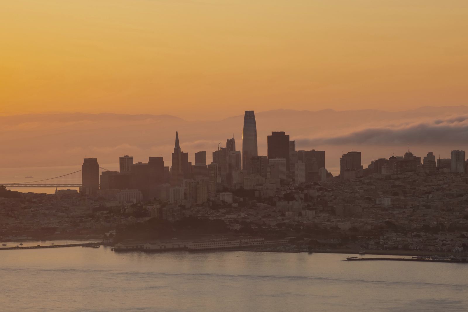 The towers of San Francisco in silhouette across the bay, under an orange sky.