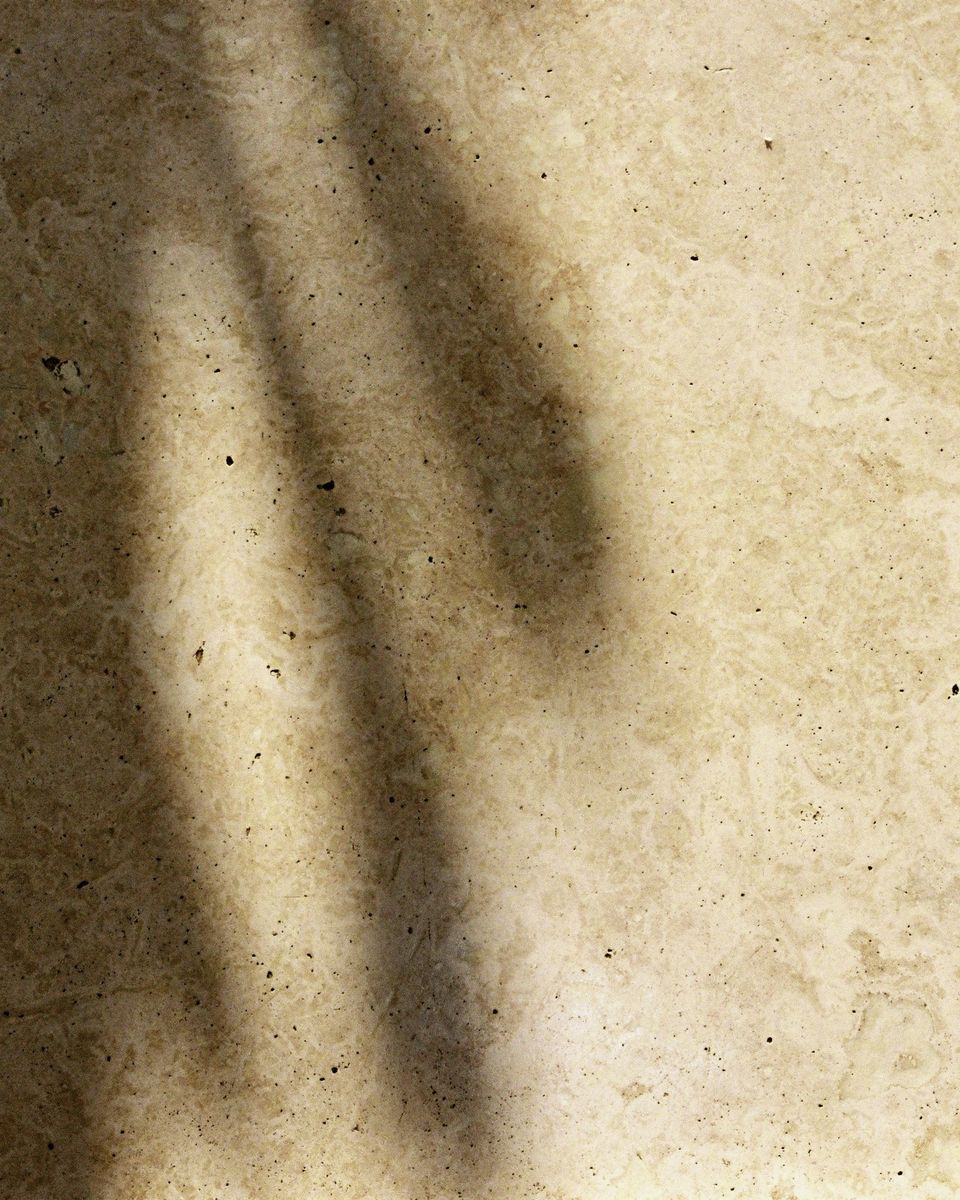 Luz suave de una ventana y sombras sobre un piso de piedra color crema.