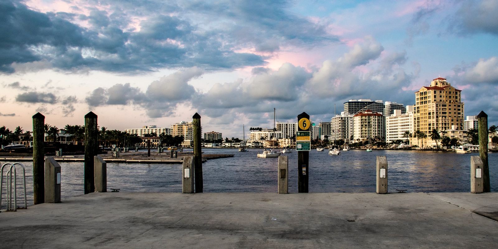 West Palm Beach al otro lado del agua al atardecer, vista desde un muelle, con barcos amarrados y torres en la orilla.